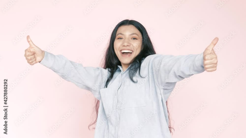 Portrait of young positive smiling happy hispanic latin woman in good mood rejoicing praise celebrating success, showing thumb up, looking at camera. Indoor studio shot isolated on pink background Portrait of young positive smiling happy hispanic latin woman in good mood rejoicing praise celebrating success, showing thumb up, looking at camera. Indoor studio shot isolated on pink background
