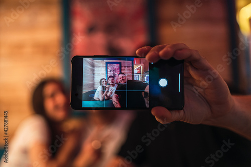 Tres amigos, dos chicos y una chica mirando smartphone y tomando selfies en un bar de decoración circense