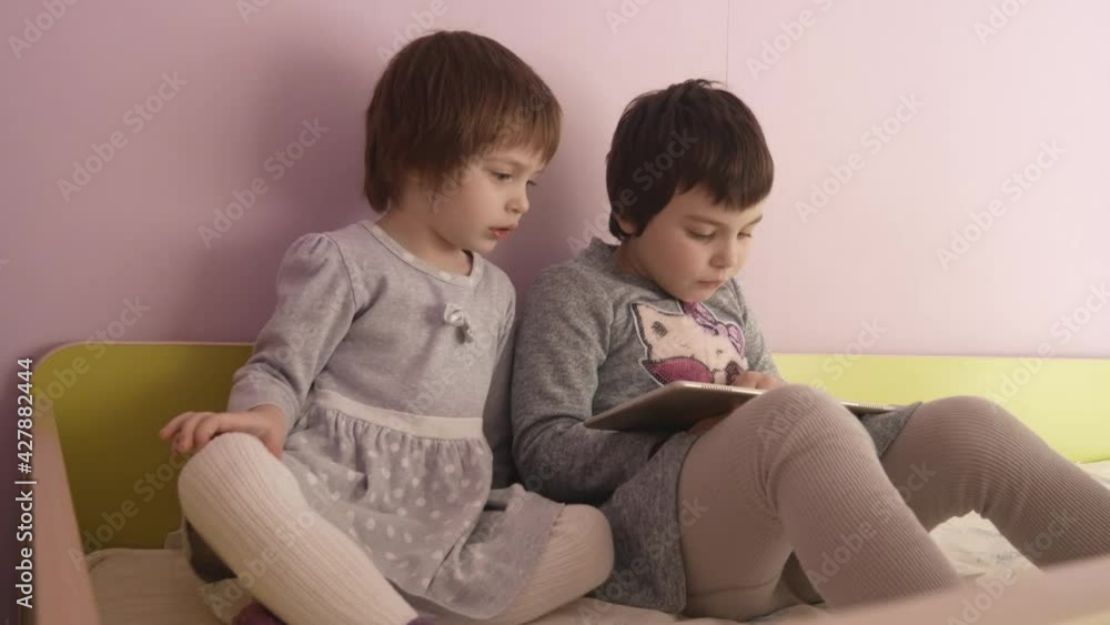 Children and gadget. Two girls are watching cartoons on a tablet. Two girls in gray dresses are playing a computer game. Children and gadget. Two girls are watching cartoons on a tablet. Two girls in gray dresses are playing a computer game.
