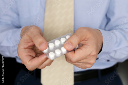 Man in office clothes taking pills, pack of medication in male hands close up. Concept of antidepressant, stress at work, vitamins, dose of drugs, flu treatment