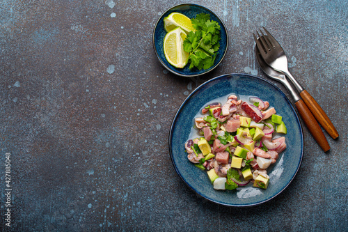 Peruvian ceviche with fresh fish, seafood, avocado on ceramic blue plate on rustic stone background from above, traditional dish of Peru cuisine with space for text photo