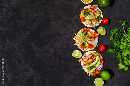 Tacos with crispy fish, avocado, guacamole sauce and lime on dark background. Top view with copy space. Mexican cuisine
