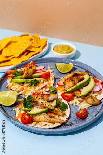 Tacos with crispy fish, avocado, guacamole sauce, nachos chips and lime. Mexican cuisine
