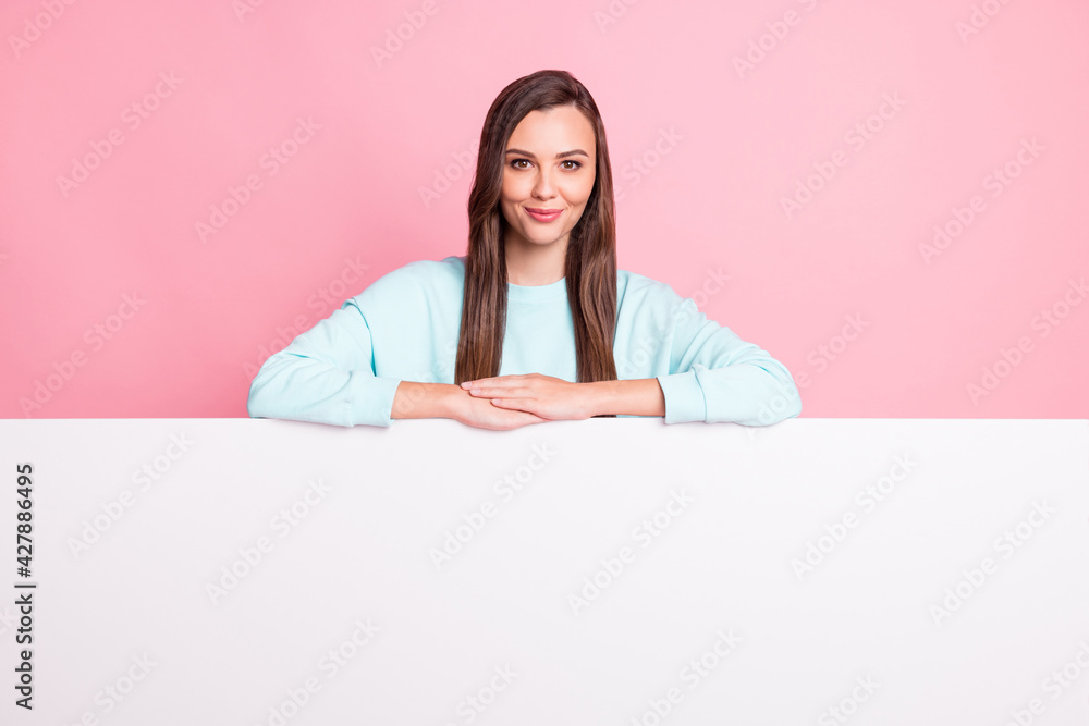 Photo of beautiful young woman wear blue sweater stand behind empty space placard isolated on pastel pink color background Photo of beautiful young woman wear blue sweater stand behind empty space placard isolated on pastel pink color background