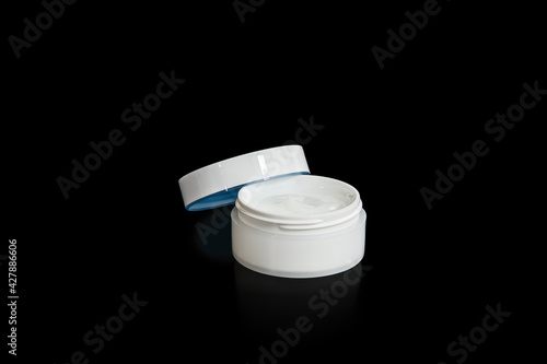 Obraz na płótnie Cosmetic jar with face cream on black background. Opened blank white cosmetic container. Facial care concept. w salonie