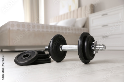 Steel dumbbell and weight plates on floor indoors. Fitness at home