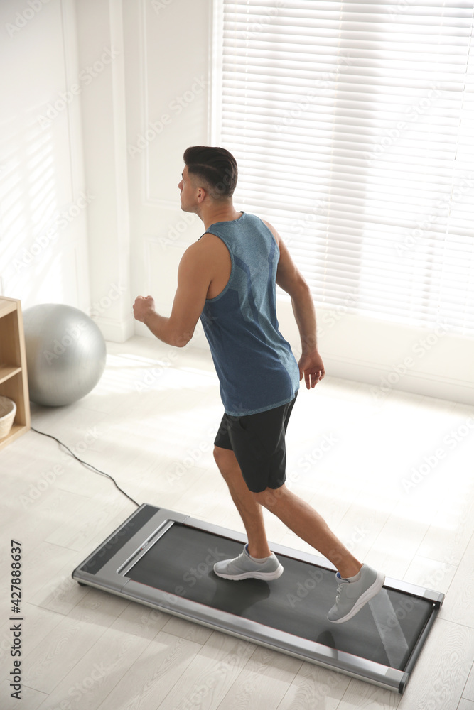 Fototapeta premium Sporty man training on walking treadmill at home