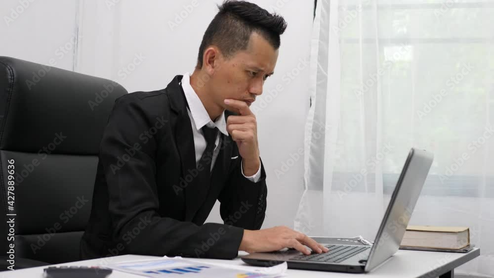 Asian businessman in looking at computer screen sitting at table at office thinking of problem solution failed business stuck Asian businessman in looking at computer screen sitting at table at office thinking of problem solution failed business stuck