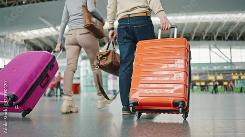 Two travellers with luggage walking to terminal at airport building, closeup up of bright suitcases