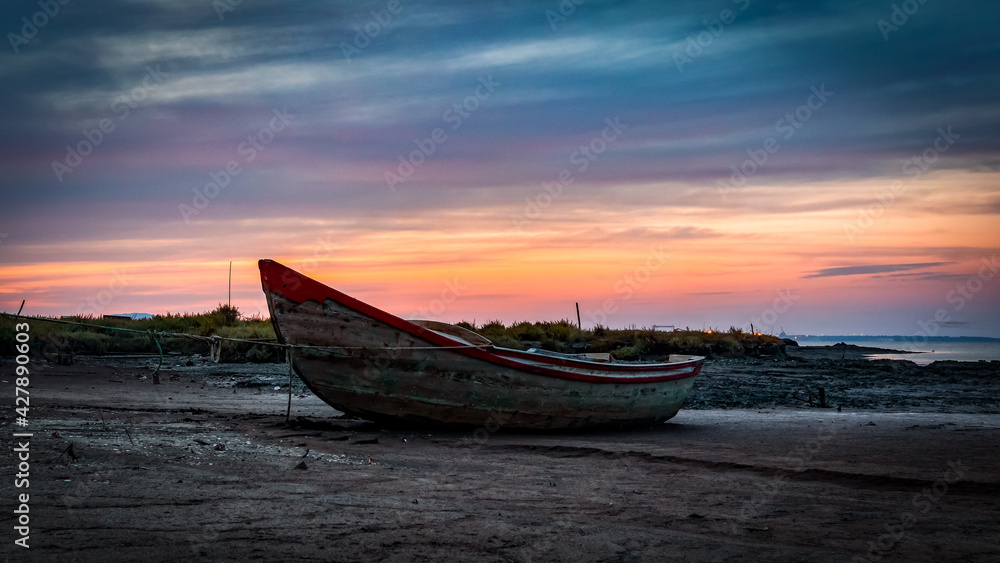 A fisherman boat on the beach at sunset next to the Carrasqueira Palafitic pier in Comporta, Portugal.