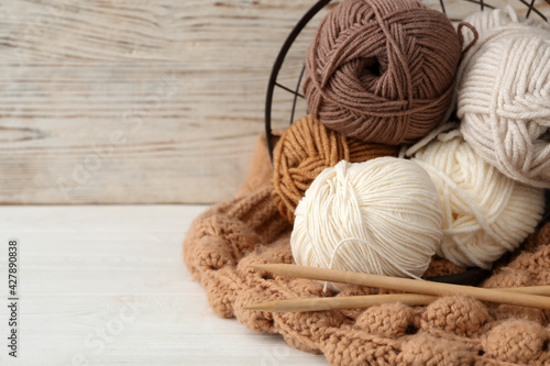 Soft woolen yarns with knitting needles and sweater on white table, closeup. Space for text