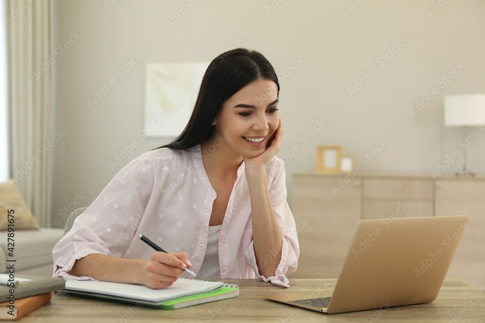 Young woman taking notes during online webinar at table indoors Young woman taking notes during online webinar at table indoors