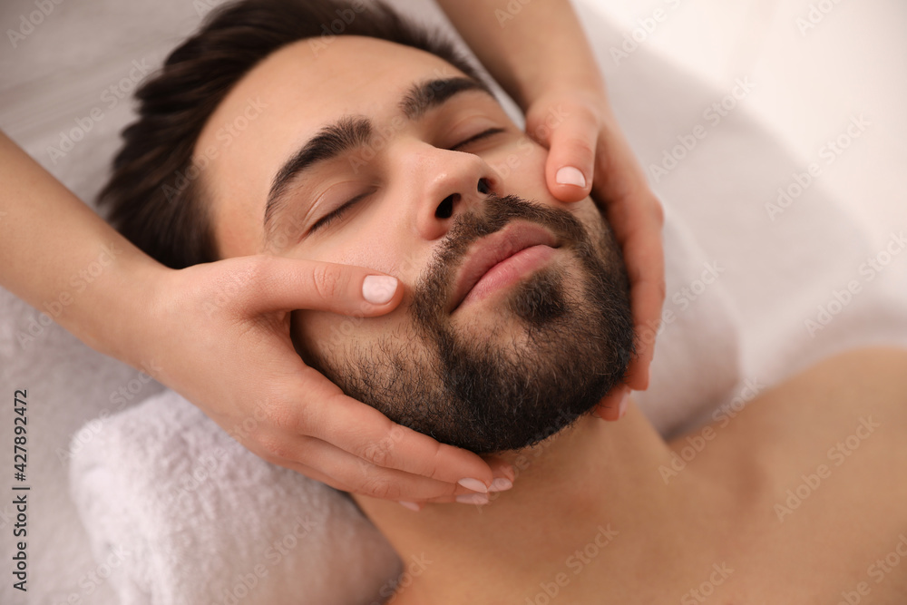 Young man receiving facial massage in beauty salon, closeup - obrazy, fototapety, plakaty 