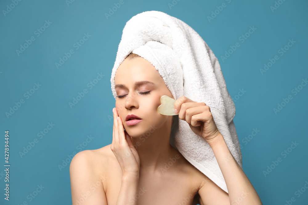 Beautiful young woman doing facial massage with gua sha tool on blue background Beautiful young woman doing facial massage with gua sha tool on blue background