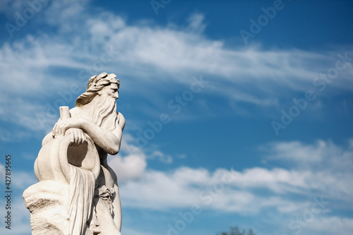 Antique statue of a man with a jug on the background of a white sky in a park close-up