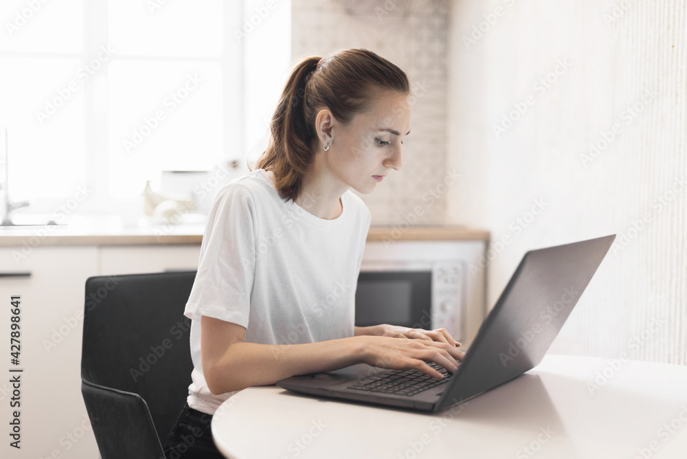 Young woman working on laptop at kitchen. Female freelancer working online Young woman working on laptop at kitchen. Female freelancer working online