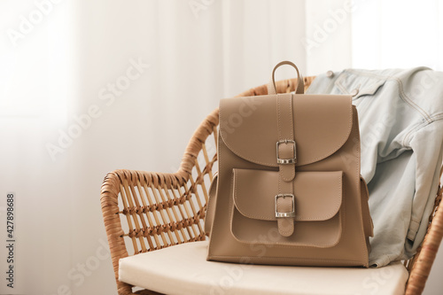 Stylish beige backpack and jacket on wicker chair indoors, space for text photo