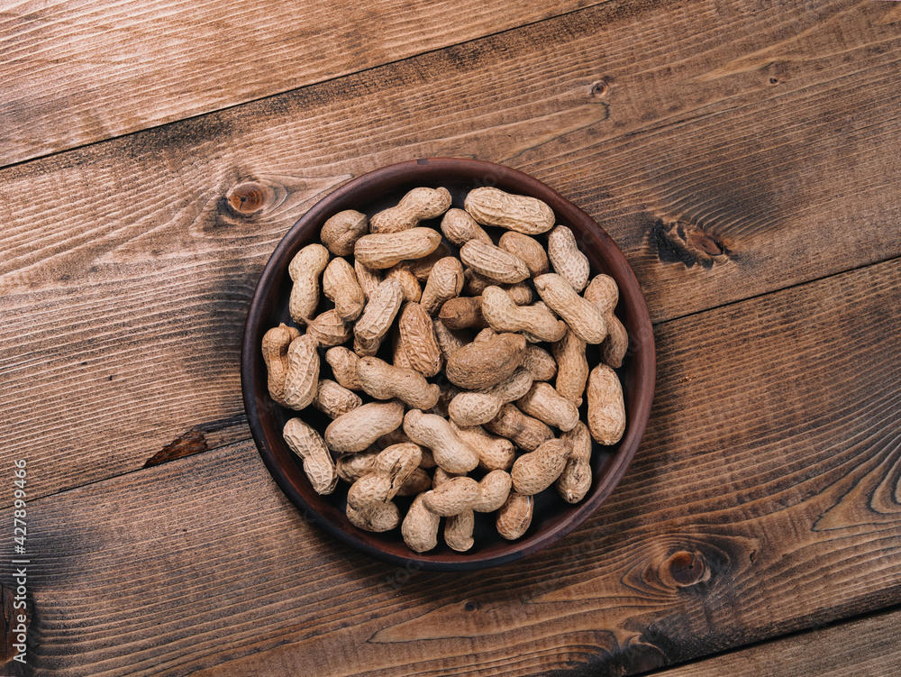 Freshly roasted peanuts on a clay plate on a wooden tabletop Freshly roasted peanuts on a clay plate on a wooden tabletop