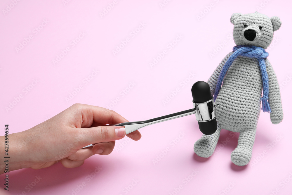 Woman pretending to test teddy bear's reflexes with hammer on pink background, closeup. Nervous system diagnostic Woman pretending to test teddy bear's reflexes with hammer on pink background, closeup. Nervous system diagnostic