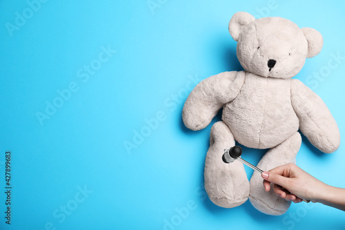 Tableau sur toile Woman pretending to test teddy bear's reflexes with hammer on light blue background, closeup and space for text