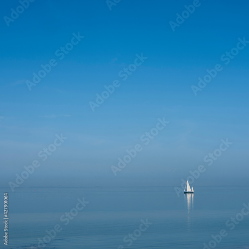 lonely sailing vessel on blue water of vast empty lake under blue sky
