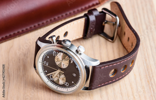 A stainless steel wristwatch with leather strap is resting on a light coloured wooden table top