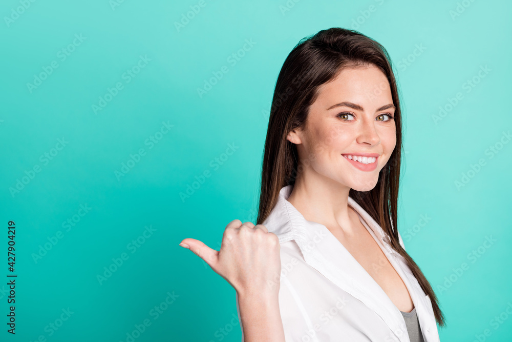Profile side photo of cheerful nice young woman point finger thumb empty space advert isolated on teal color background Profile side photo of cheerful nice young woman point finger thumb empty space advert isolated on teal color background