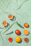 Summer scene with fruits,rosemary and glasses of water or lemonade on pastel green beach towel. Drinks and refreshment concept. Sunlit flat lay. Minimal style. Top view.