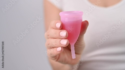 A faceless woman wearing a white T-shirt holds a pink menstrual cup with red liquid inside photo
