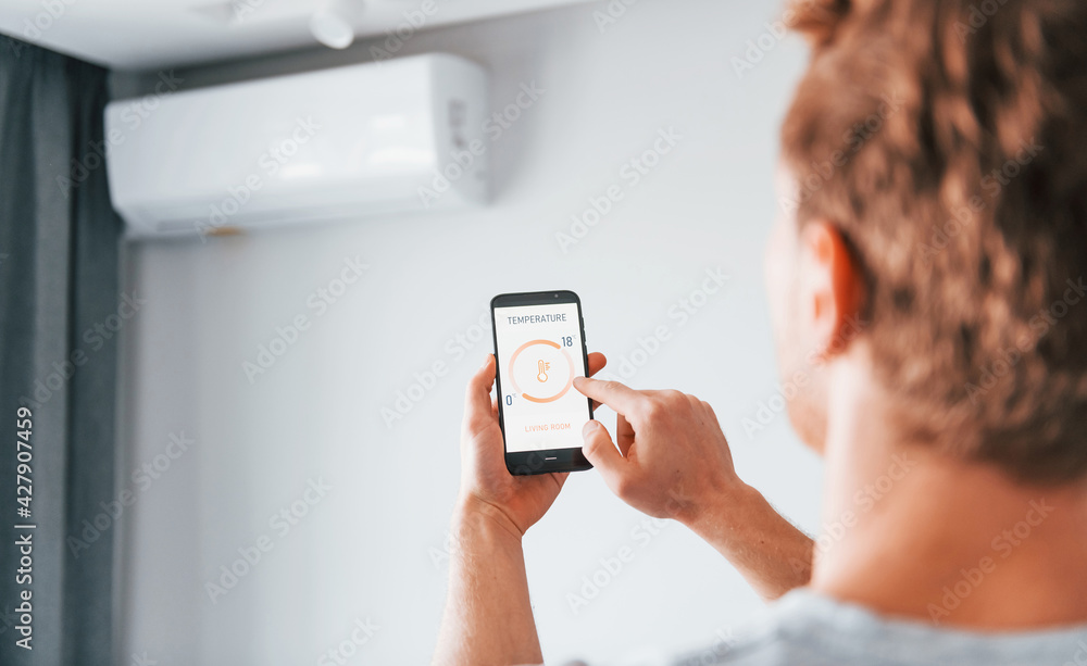 Rear view of adult man that is indoors controlling smart home technology Rear view of adult man that is indoors controlling smart home technology