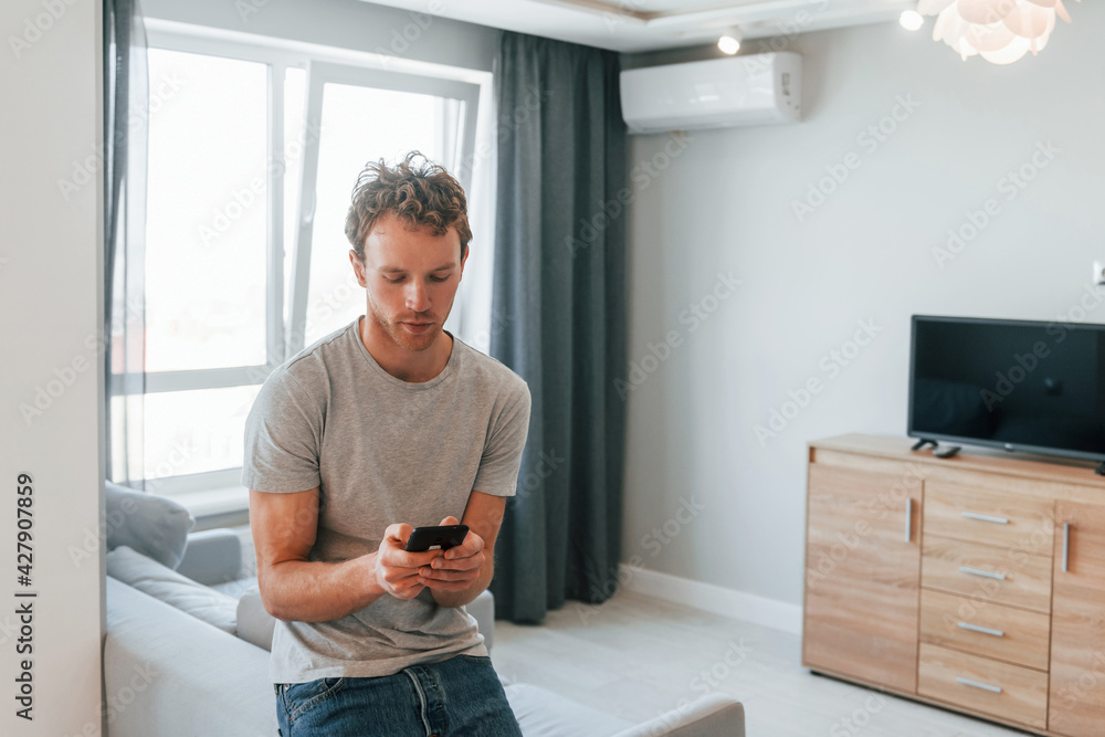 Young man in casual clothes is indoors controlling smart home technology Young man in casual clothes is indoors controlling smart home technology
