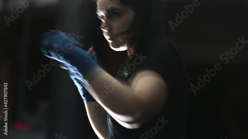 young female boxer wraps bandages around her arms and hits a punching bag. photo