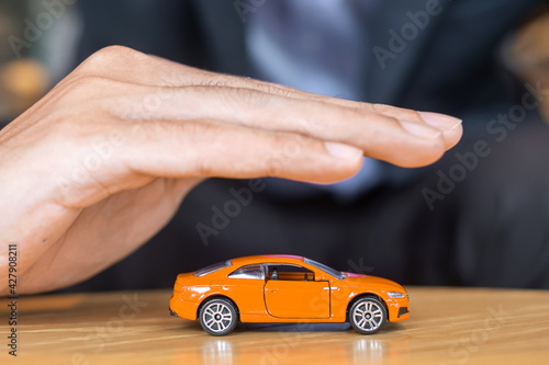 Businessman hand cover or protection orange car toy on table. Financial, money, refinance and Car insurance concept