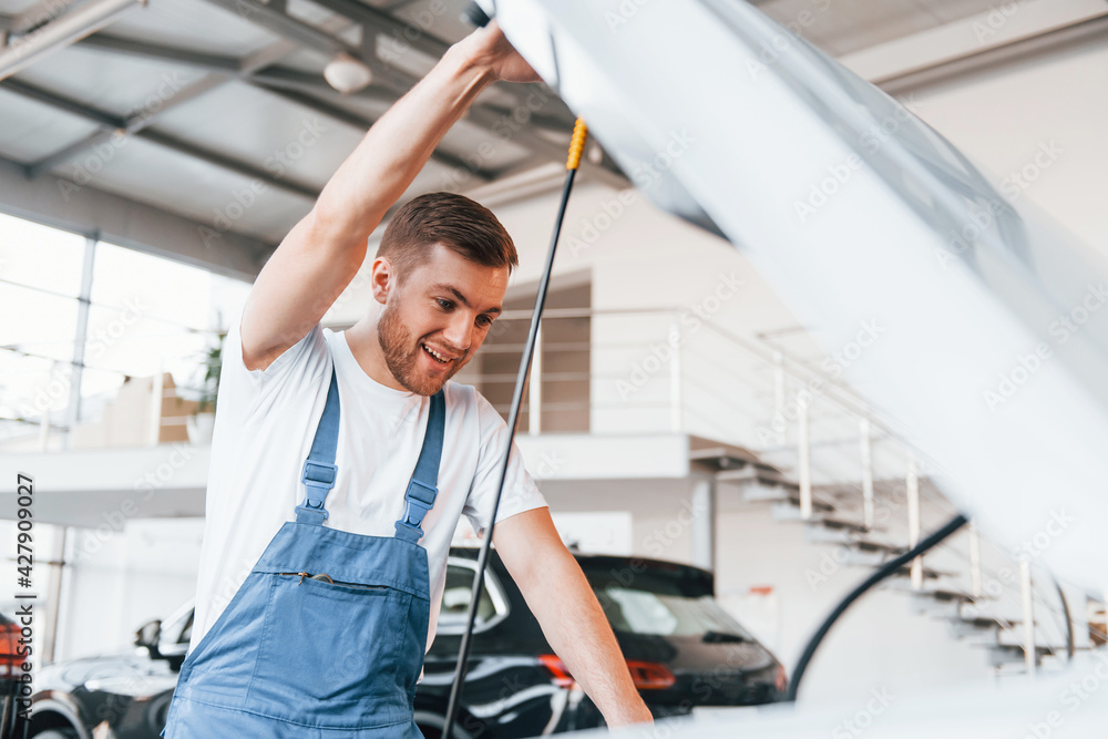 Young man in white shirt and blue uniform repairs automobile Young man in white shirt and blue uniform repairs automobile