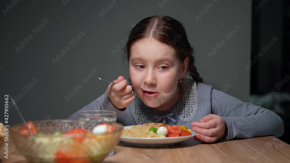 Little beautiful girl is eating in the kitchen. She sits on a chair at the table. The child eats pasta with a fresh salad of tomato, pepper and round cheese. 4K Little beautiful girl is eating in the kitchen. She sits on a chair at the table. The child eats pasta with a fresh salad of tomato, pepper and round cheese. 4K