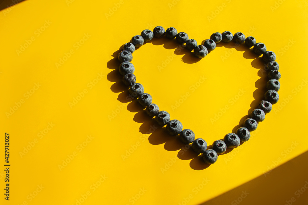 Obraz premium Healthy food, raw food diet. Blueberries in the shape of a heart on a yellow background. Hard shadows. Love symbol.