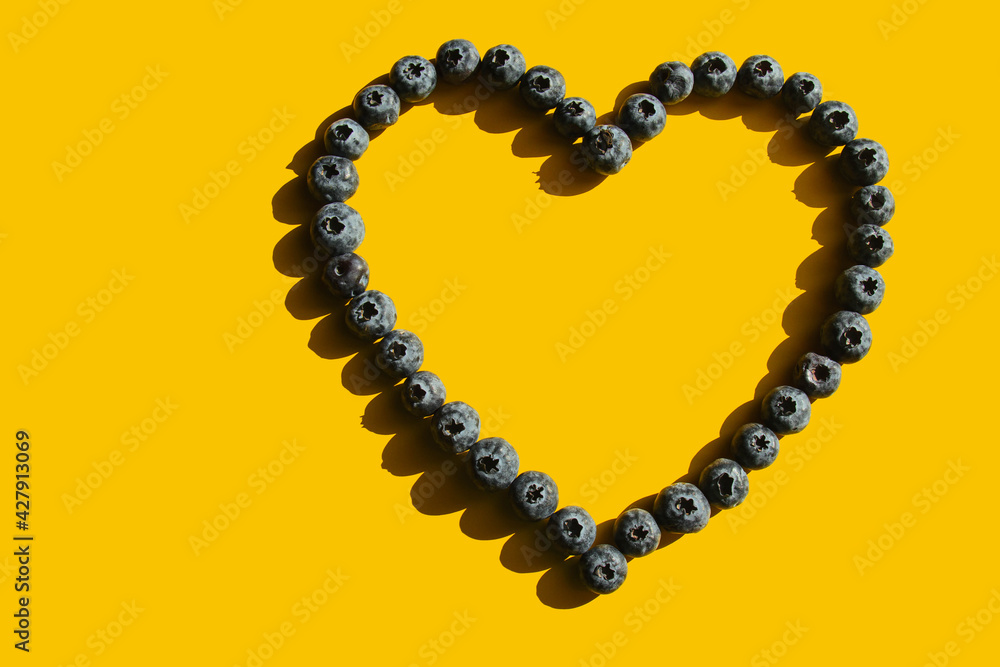 Obraz premium Healthy eating. In the sunshine. Blueberries in the shape of a heart on a yellow background. Hard shadows. Love of raw food.