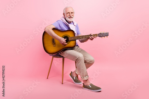 Full length body size grandpa playing guitar sitting on chair isolated on pastel pink color background