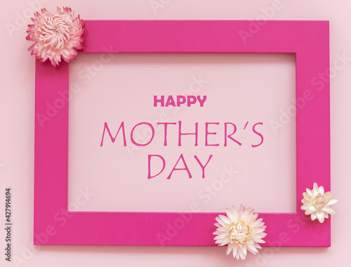 Creative arrangement of flowers on pink background with happy Mothers day text. Flat lay. © lusyaya