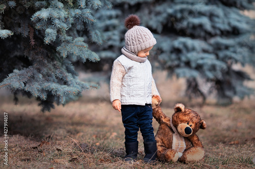 Baby and his friend bear in the park. Winnie the Pooh. Spring walk of a child with a toy. Based on a fairy tale. Brown teddy bear and a boy in a knitted hat and jacket