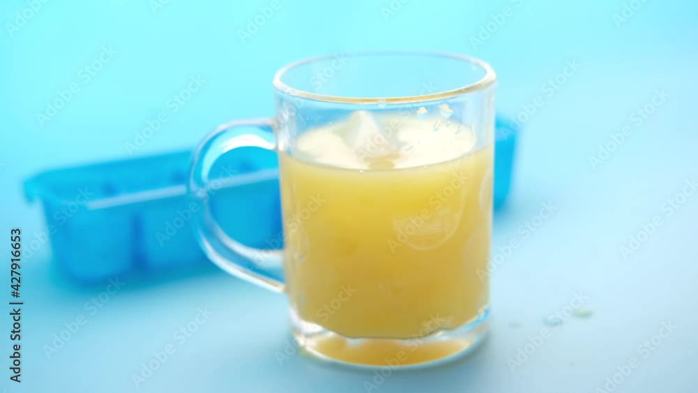 dropping ice into a glass of orange juice on blue background dropping ice into a glass of orange juice on blue background