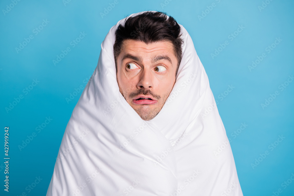 Photo portrait of scared terrified man looking to side wrapped in blanket isolated on vivid blue colored background Photo portrait of scared terrified man looking to side wrapped in blanket isolated on vivid blue colored background