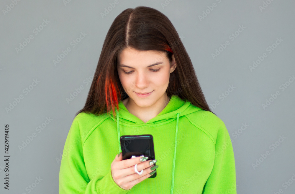 Smiling woman using smartphone over gray background. Wearing green hoodie Smiling woman using smartphone over gray background. Wearing green hoodie