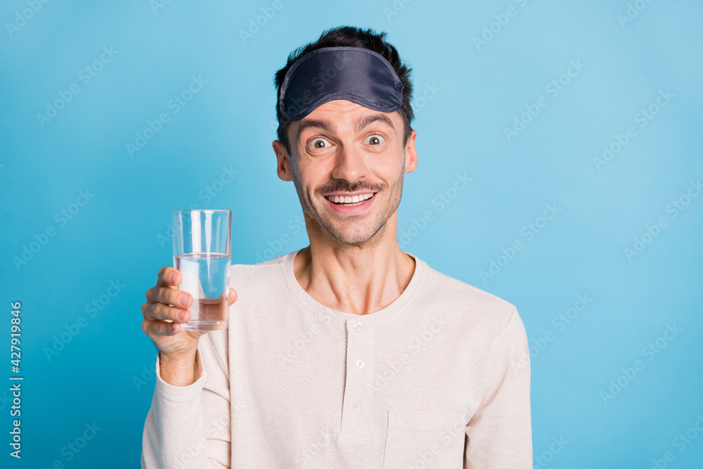 Photo portrait of excited guy holding water glass in one hand isolated on vivid blue colored background Photo portrait of excited guy holding water glass in one hand isolated on vivid blue colored background