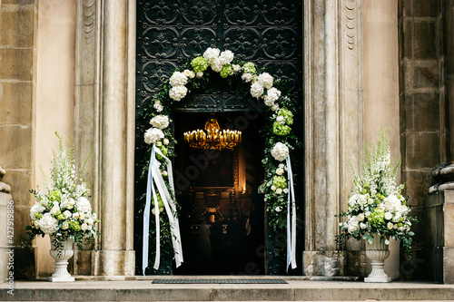 Church door decorated with beautiful white flowers and ribbons during wedding ceremony
