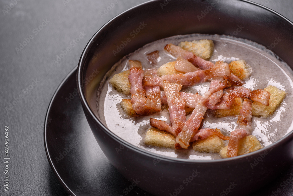 Fresh delicious hot puree soup with mushrooms and bacon in a black plate Fresh delicious hot puree soup with mushrooms and bacon in a black plate