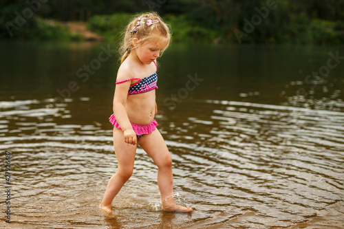 Fototapeta Naklejka Na Ścianę i Meble -  Little cute girl have fun playing with a spray of water in the river at summer. copy space