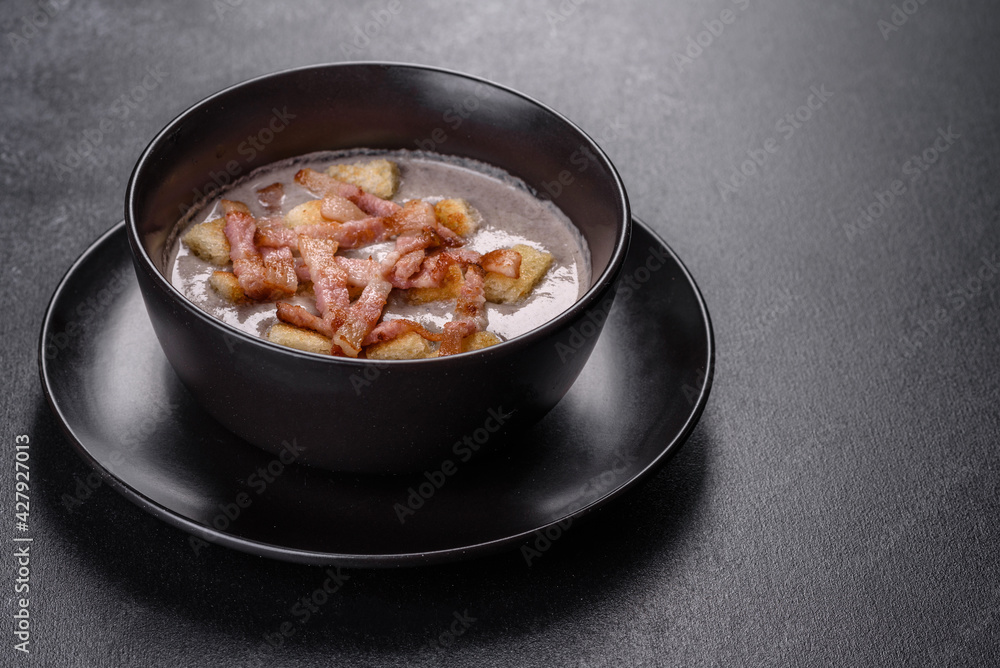Fresh delicious hot puree soup with mushrooms and bacon in a black plate Fresh delicious hot puree soup with mushrooms and bacon in a black plate