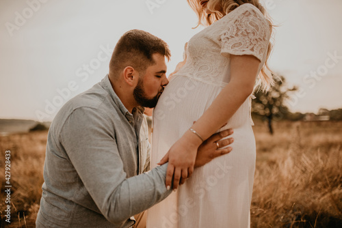 husband hugs pregnant wife hold hands on big round tummy kissing belly.