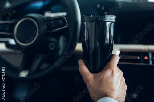 A man holding a thermo mug while driving an expensive car 